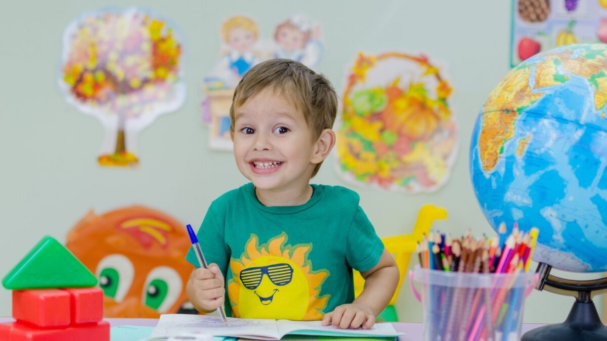 chłopak siedzi za stołem, obok niego globus, kredki i farby